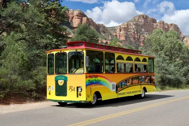 A yellow bus is driving down a road with mountains in the background.
