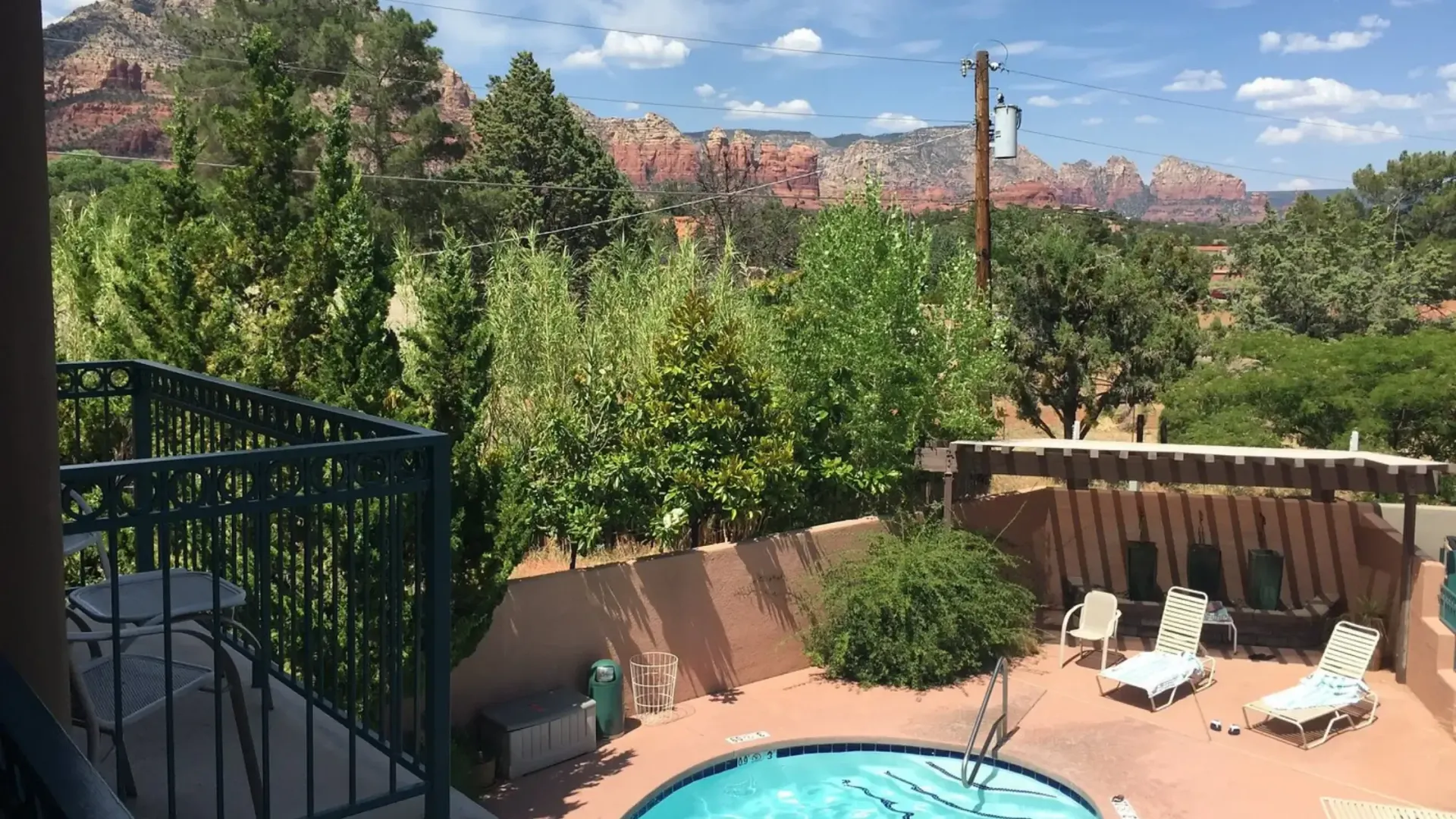 View of red rock mountains from balcony, overlooking a pool and patio with lounge chairs and trees.