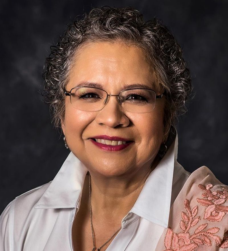 A woman wearing glasses and a white shirt is smiling for the camera.