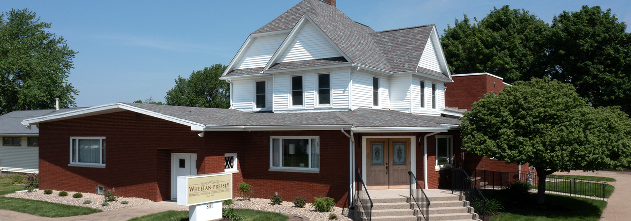 A brick and white two-story building with a red extension under a blue sky.