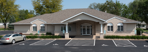 Exterior view of a one-story brick building with a car parked in front of it and a handicapped parking spot.
