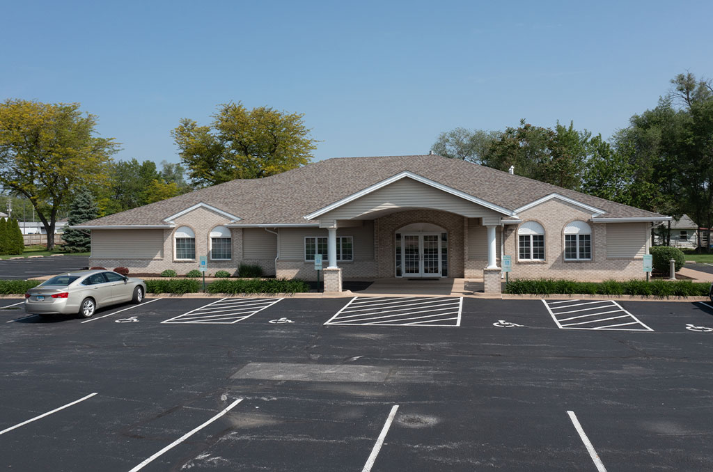 A light brick building with a parking lot and a car parked in front.