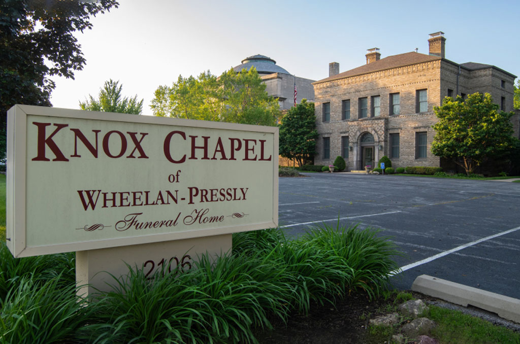 Sign for Knox Chapel of Whelan-Pressly Funeral Home, two-story stone building in background.