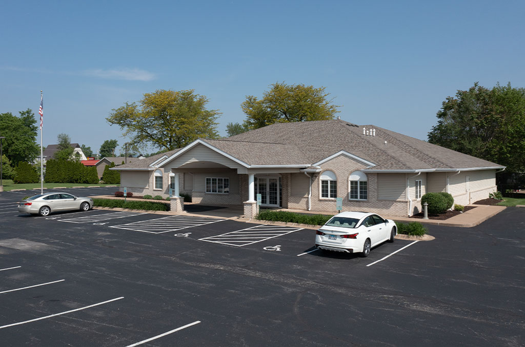 A one-story building with a parking lot and two cars. An American flag is visible.