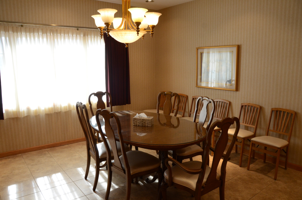 Dining room with oval table, chairs, chandelier, and a window with curtains.
