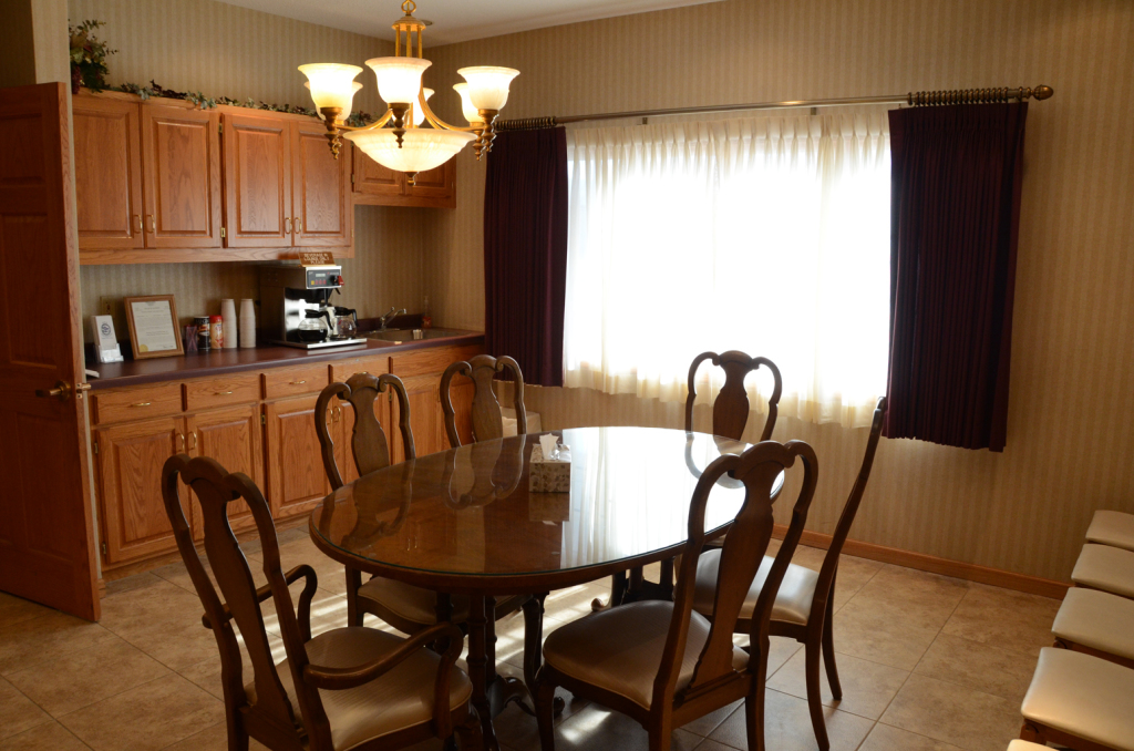 Dining room with oval table, six chairs, wooden cabinets, window with curtains, and chandelier.