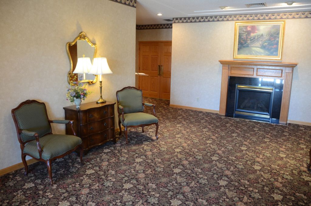 Lounge area with ornate chairs, fireplace, mirror, lamp, and floral carpet.