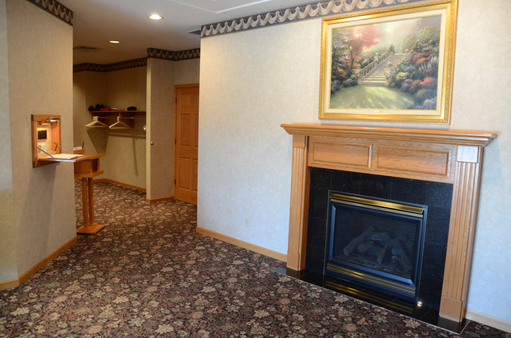 Hallway with fireplace, painting, and floral patterned carpet. A small table sits next to a wall-mounted display.