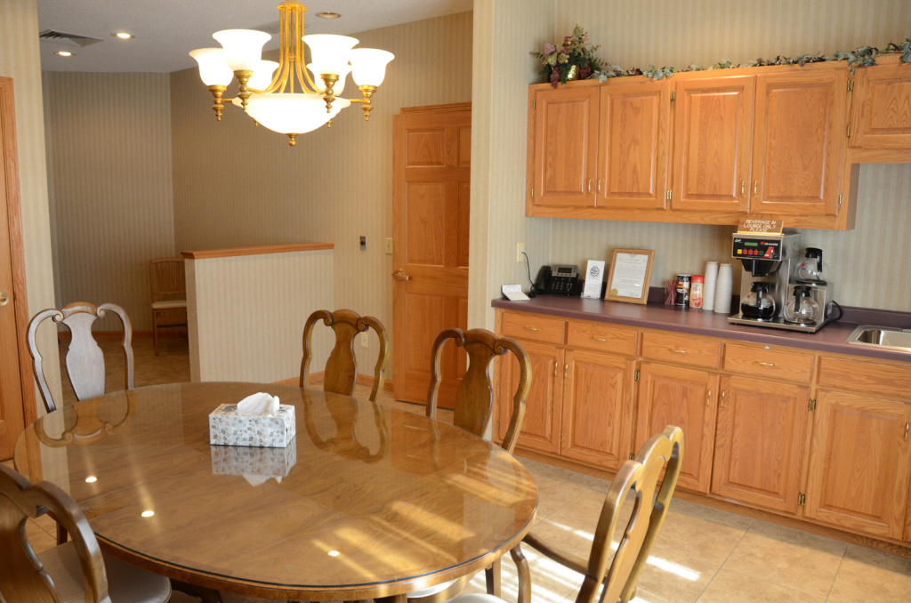 Dining room with oval wooden table, chairs, and light wood cabinetry. Chandelier hangs overhead.