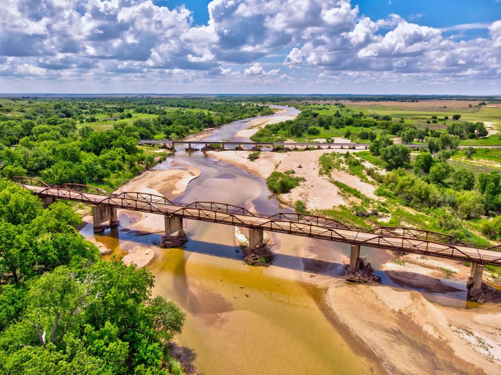 An aerial view of a bridge over a river surrounded by trees.