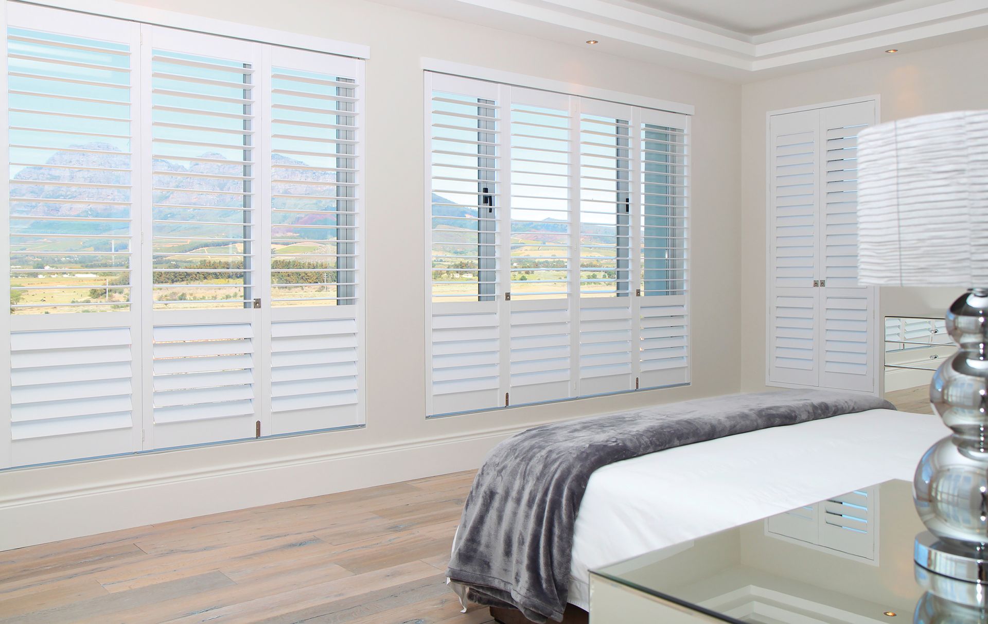 Bedroom with white shutters on large windows overlooking a scenic landscape