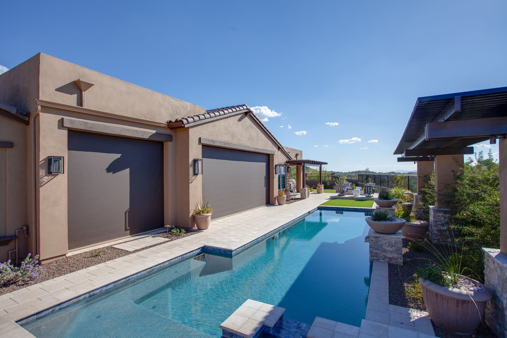 Poolside view of a house with a lap pool, external shades, and patio with a blue sky.