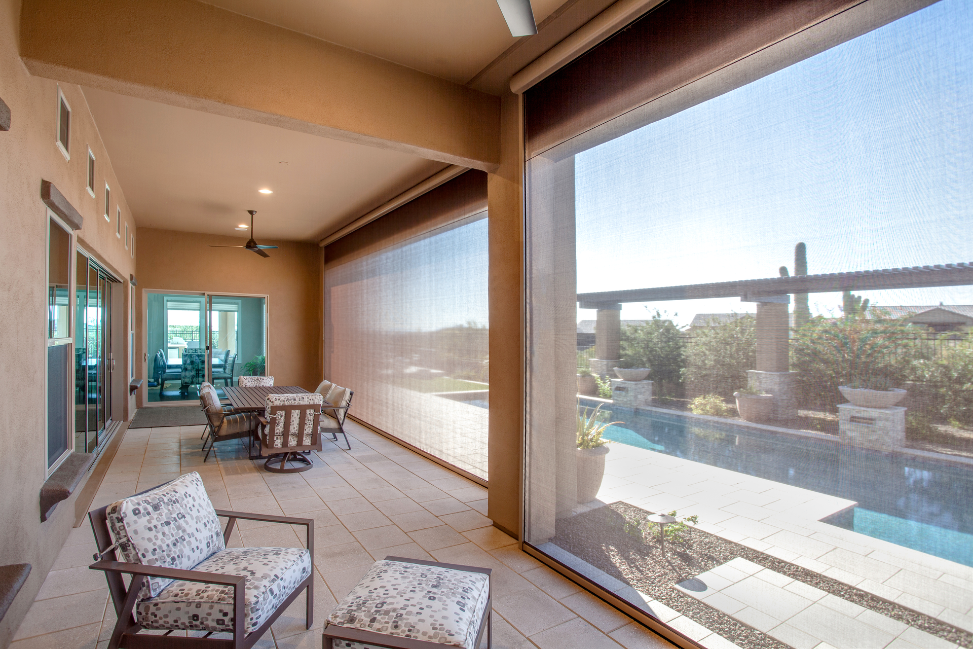 Patio with seating, dining table, and pool view, partially shaded by screens.