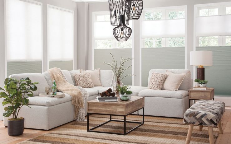 Cozy living room with sectional sofa, coffee table, and patterned rug. Windows with light-colored blinds.