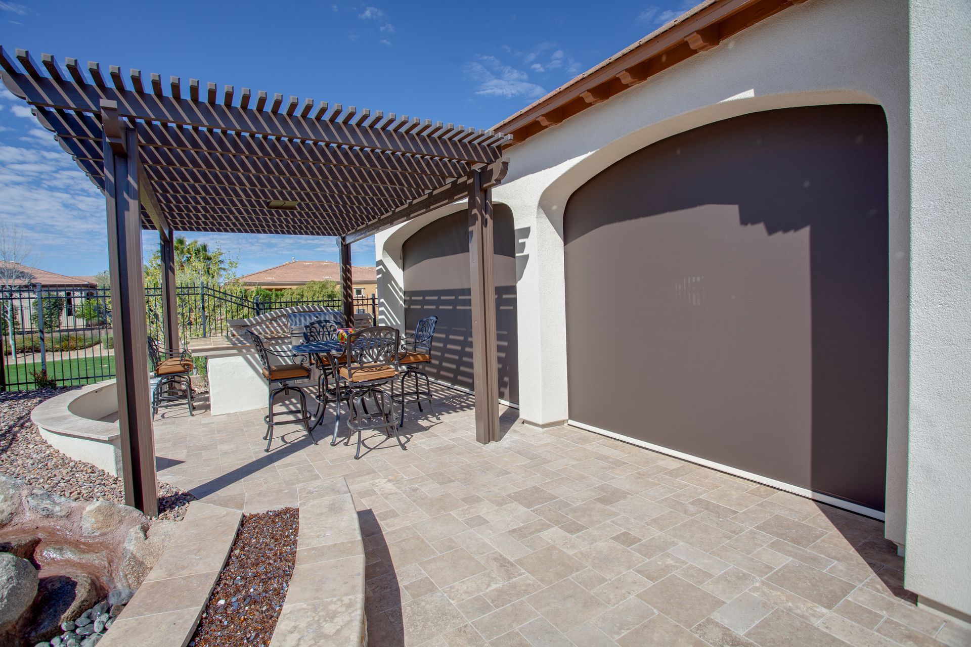 Patio with pergola, seating, and a large brown screen shade attached to the house.
