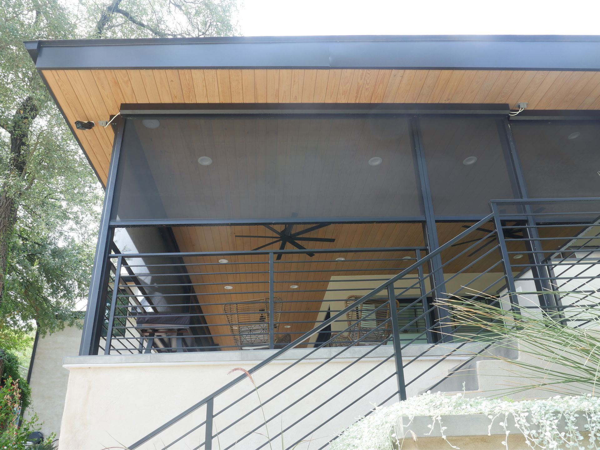 Screened-in porch with external black shades, metal railings, and wooden ceiling.