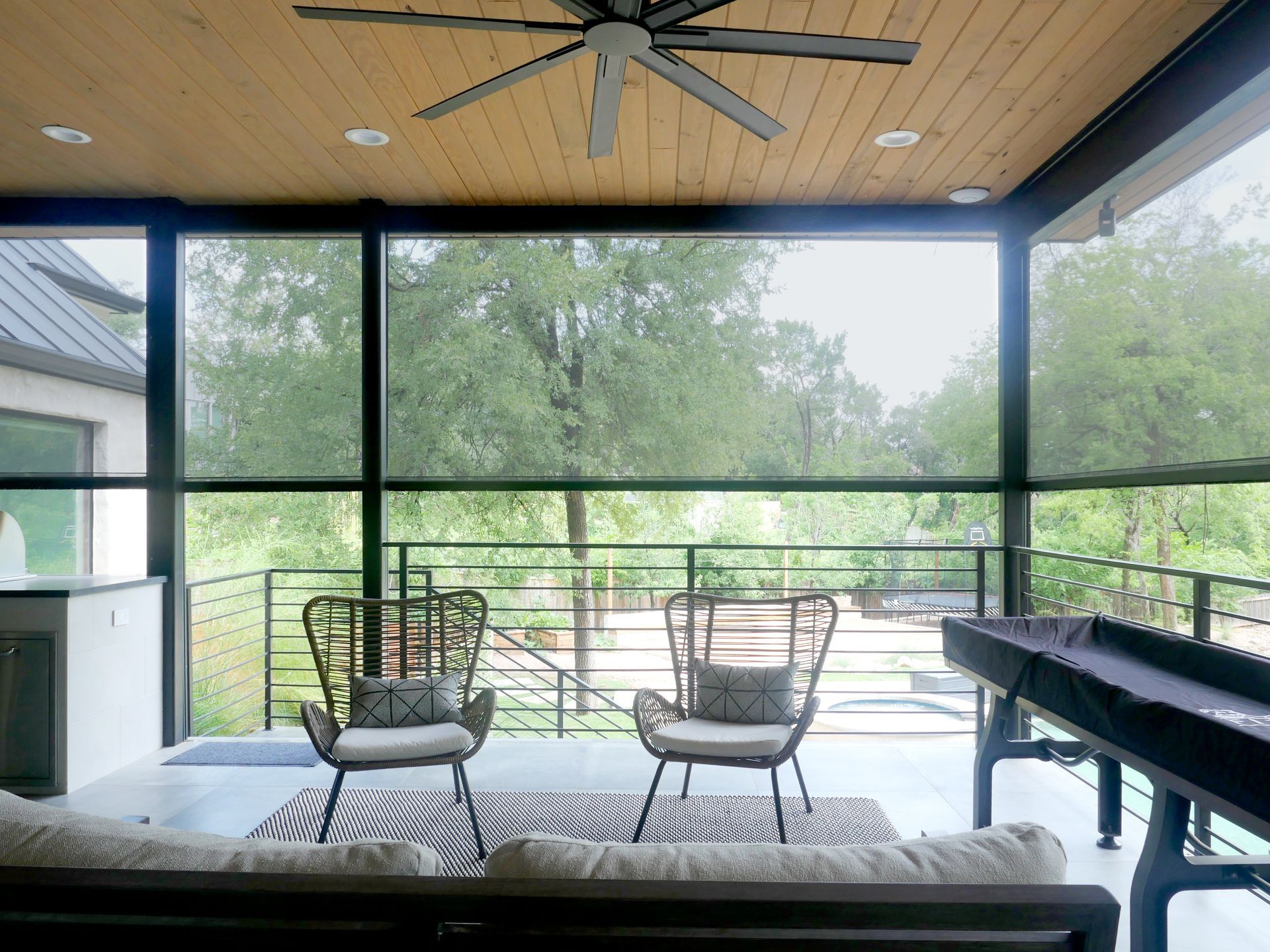 Screened-in porch with chairs, rug, and shuffleboard table with outdoor shades