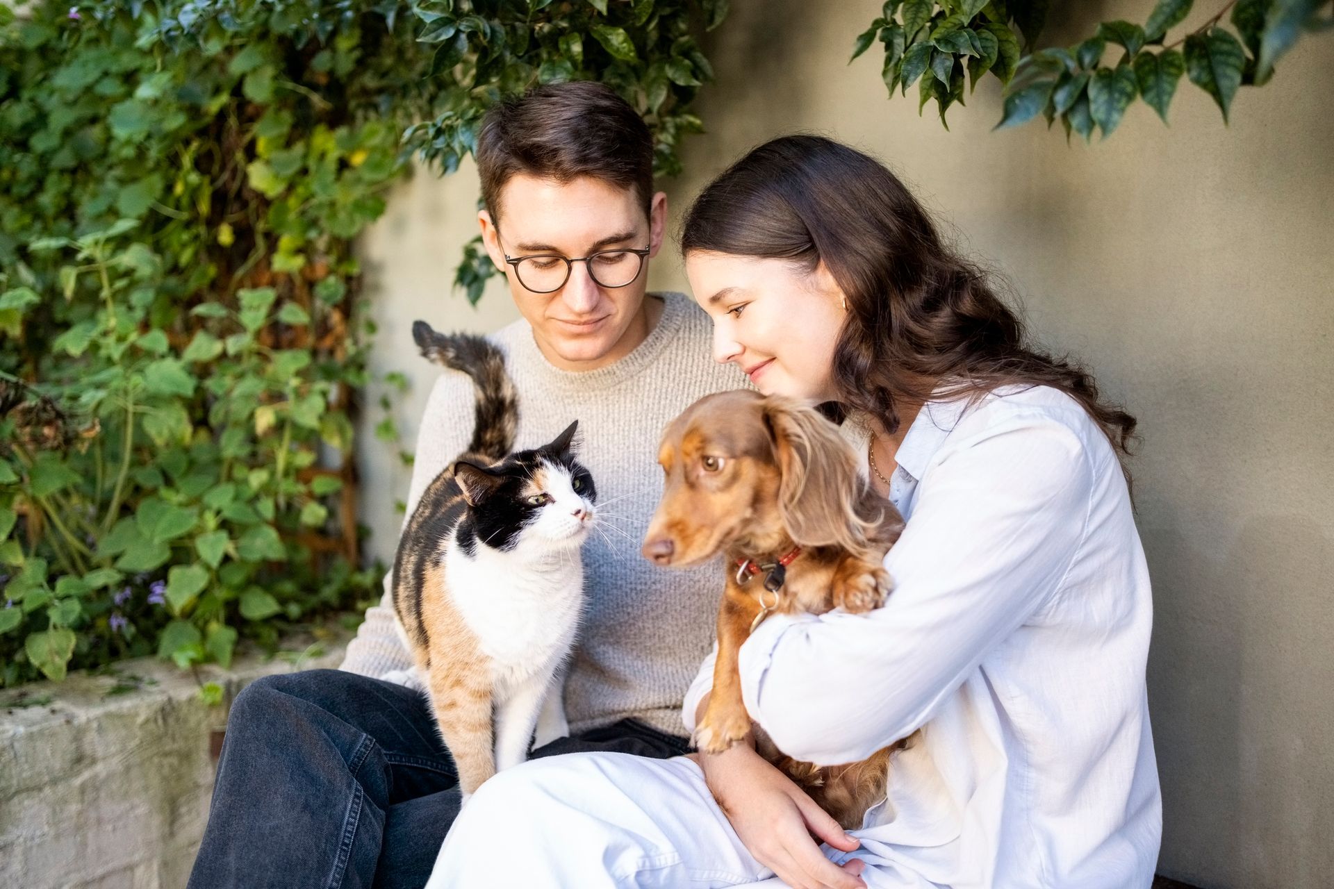 A man and a woman are sitting next to a cat and a dog.