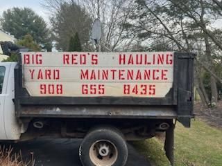 A dump truck with a sign on the back that says big red 's hauling yard maintenance