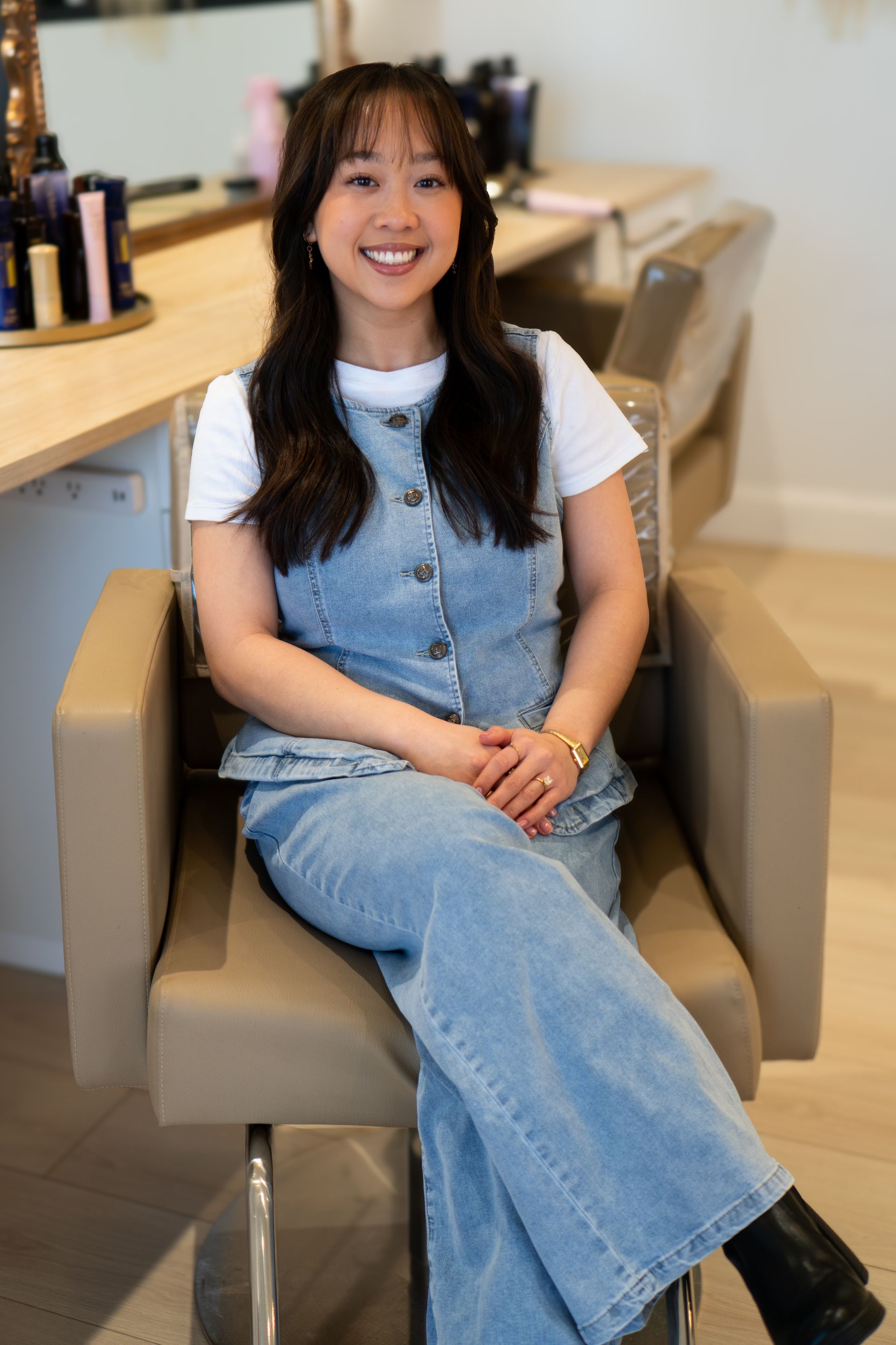 Woman in denim outfit smiles, seated in a salon chair.