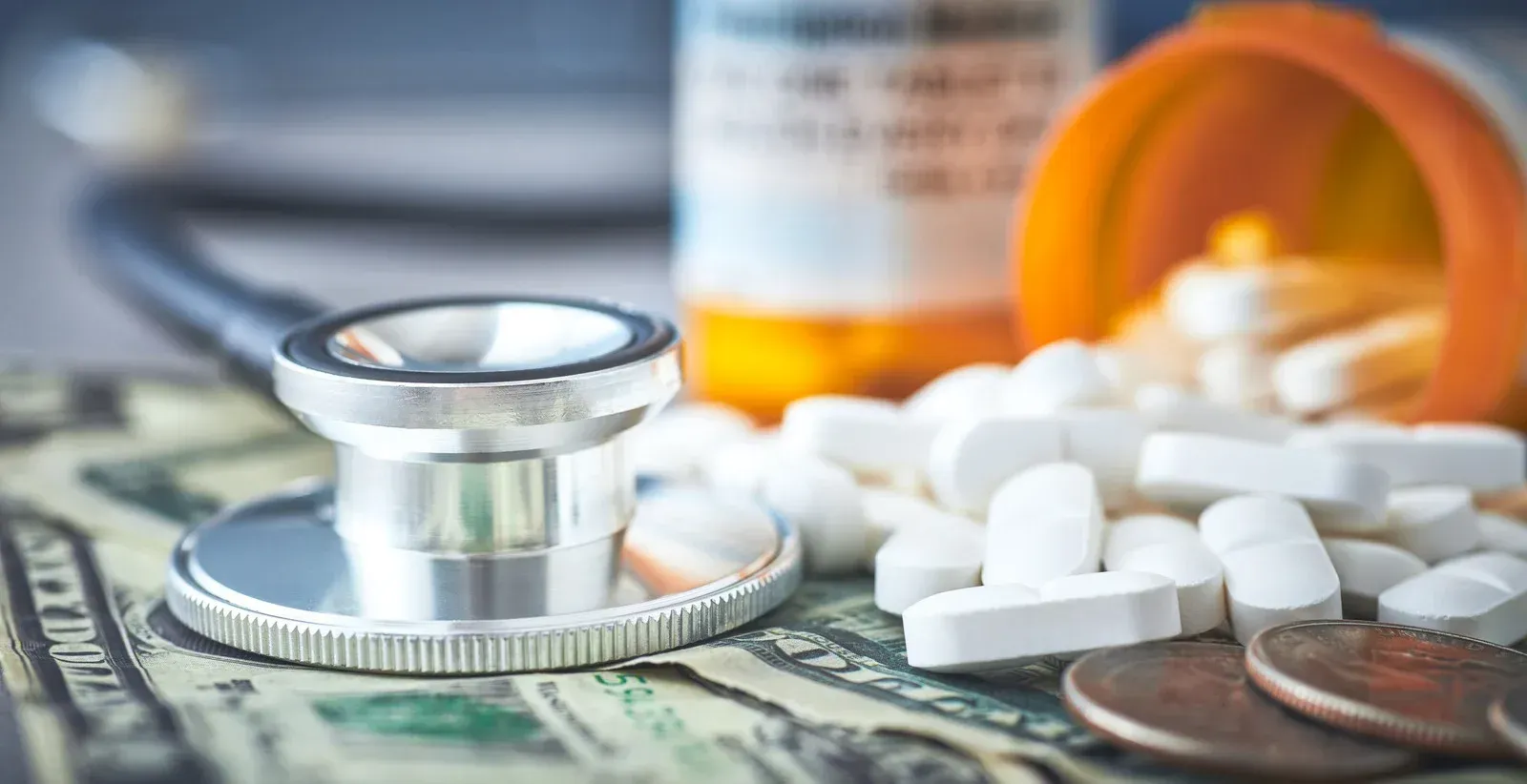A stethoscope is sitting on top of a pile of money next to a bottle of pills.