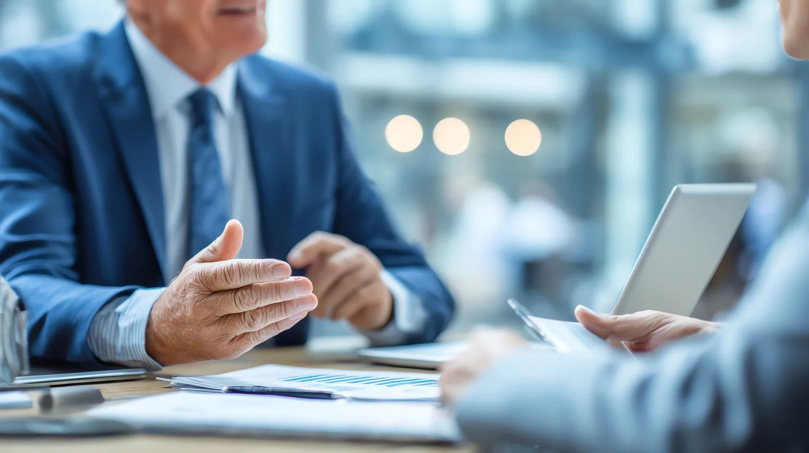 Business meeting with two people in suits discussing documents at a table in a bright office