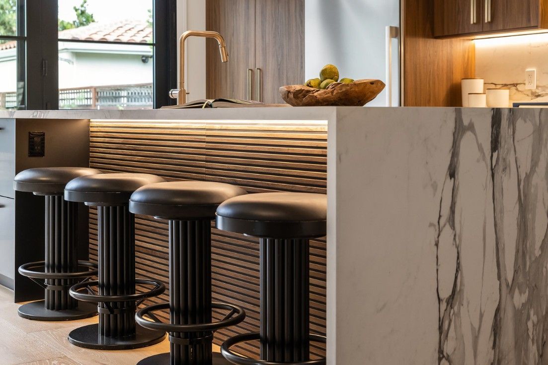 Kitchen bar with black stools, textured wall, marble countertop, and gold faucet.