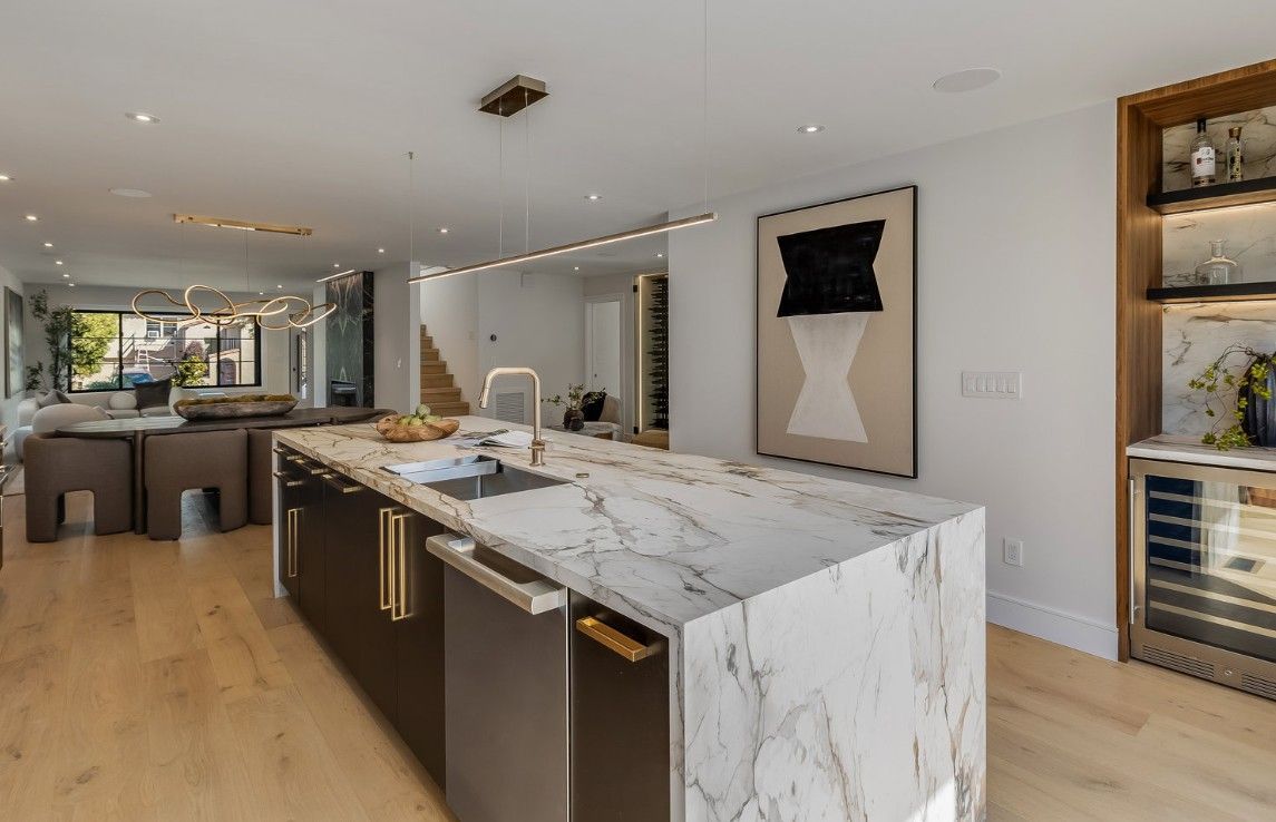 Modern kitchen with large marble island, wood flooring, and artwork on the wall.