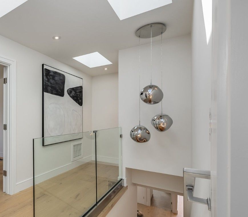 Hallway with glass railing, modern art, and silver pendant lights.