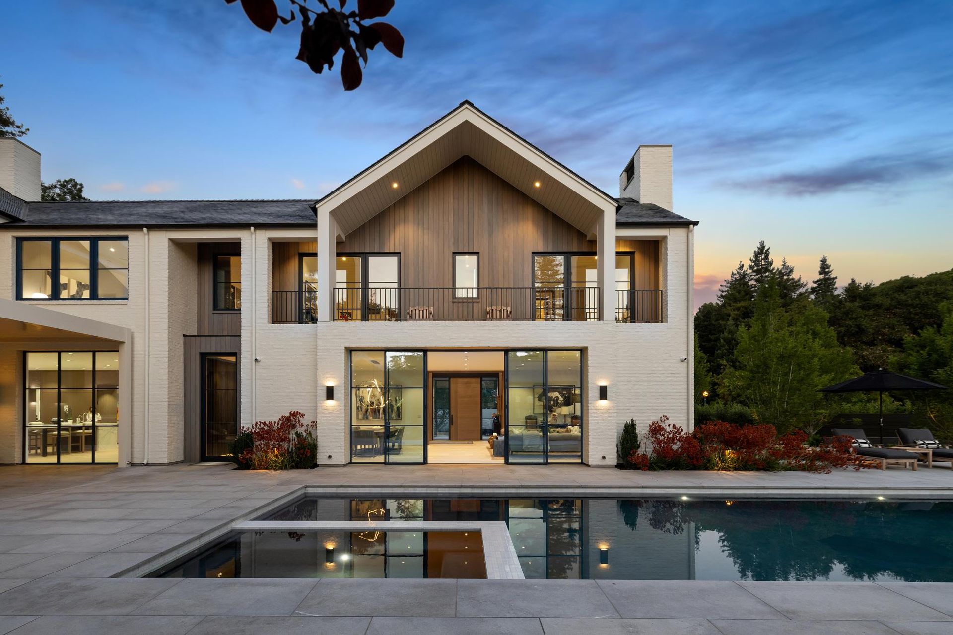 Luxury home with pool reflecting the house; white exterior, wood accents, and evening sky.