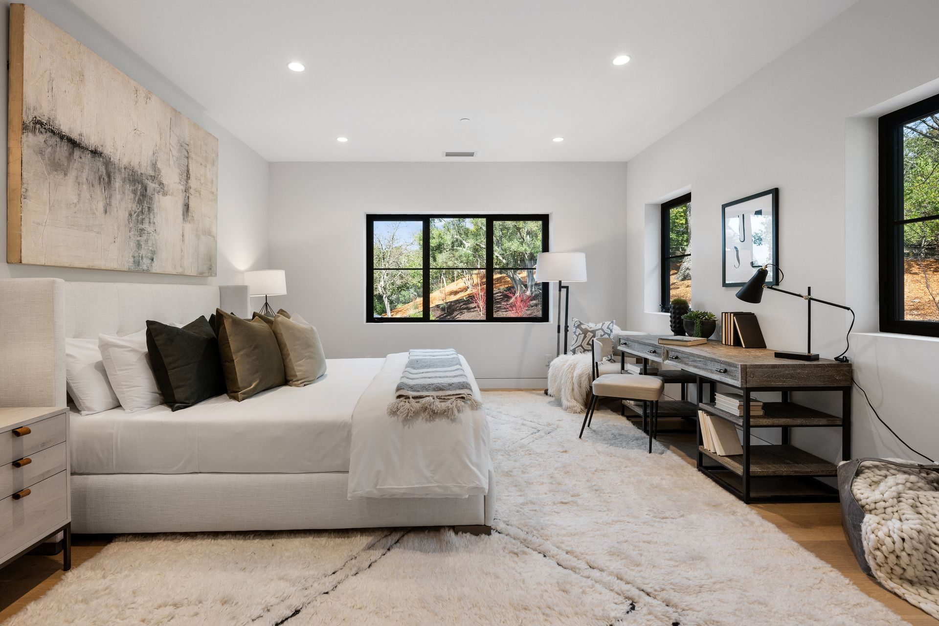 A bedroom with a large bed , desk , chair and two windows.