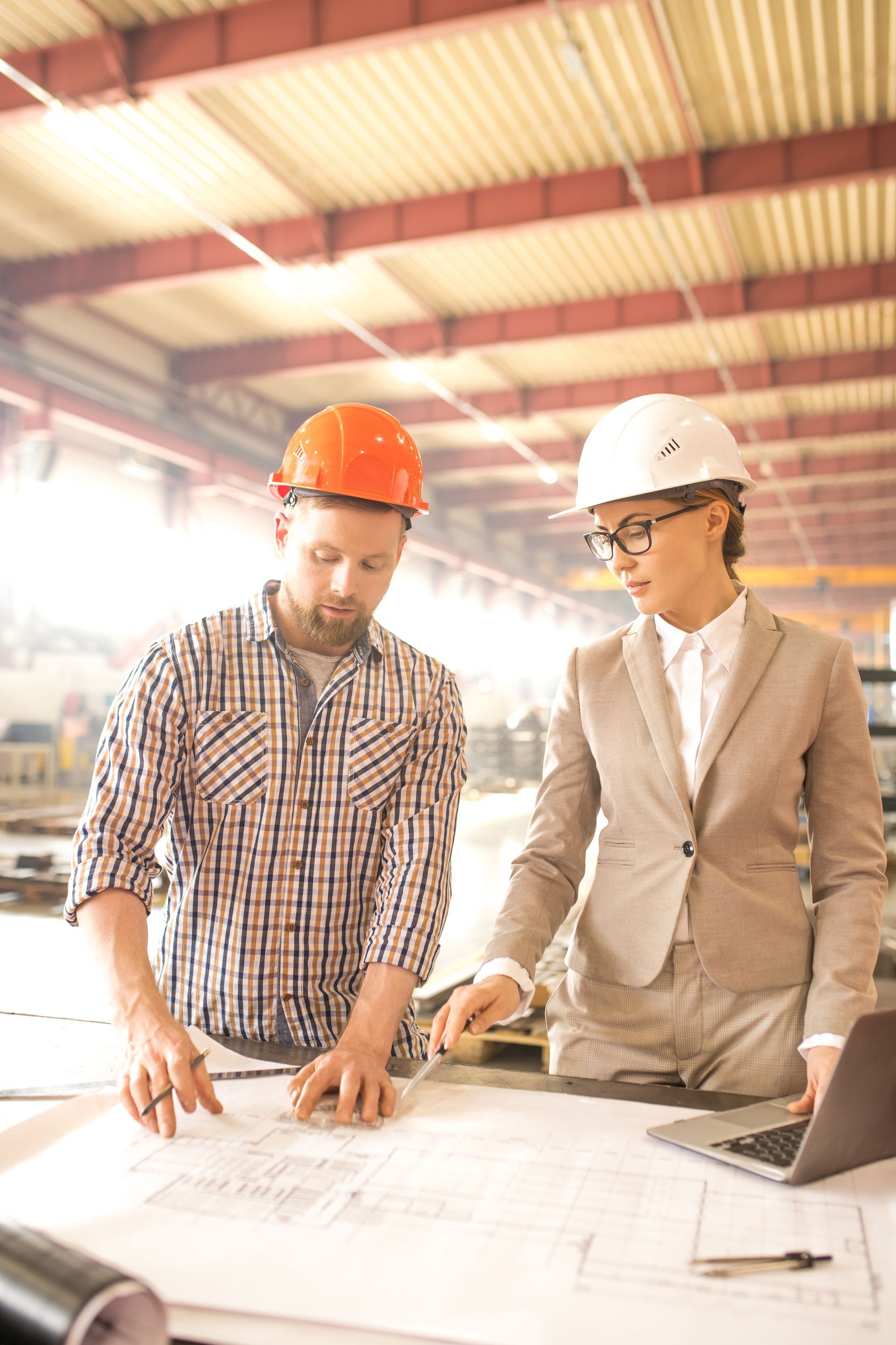 A man and a woman are looking at a blueprint in a factory.