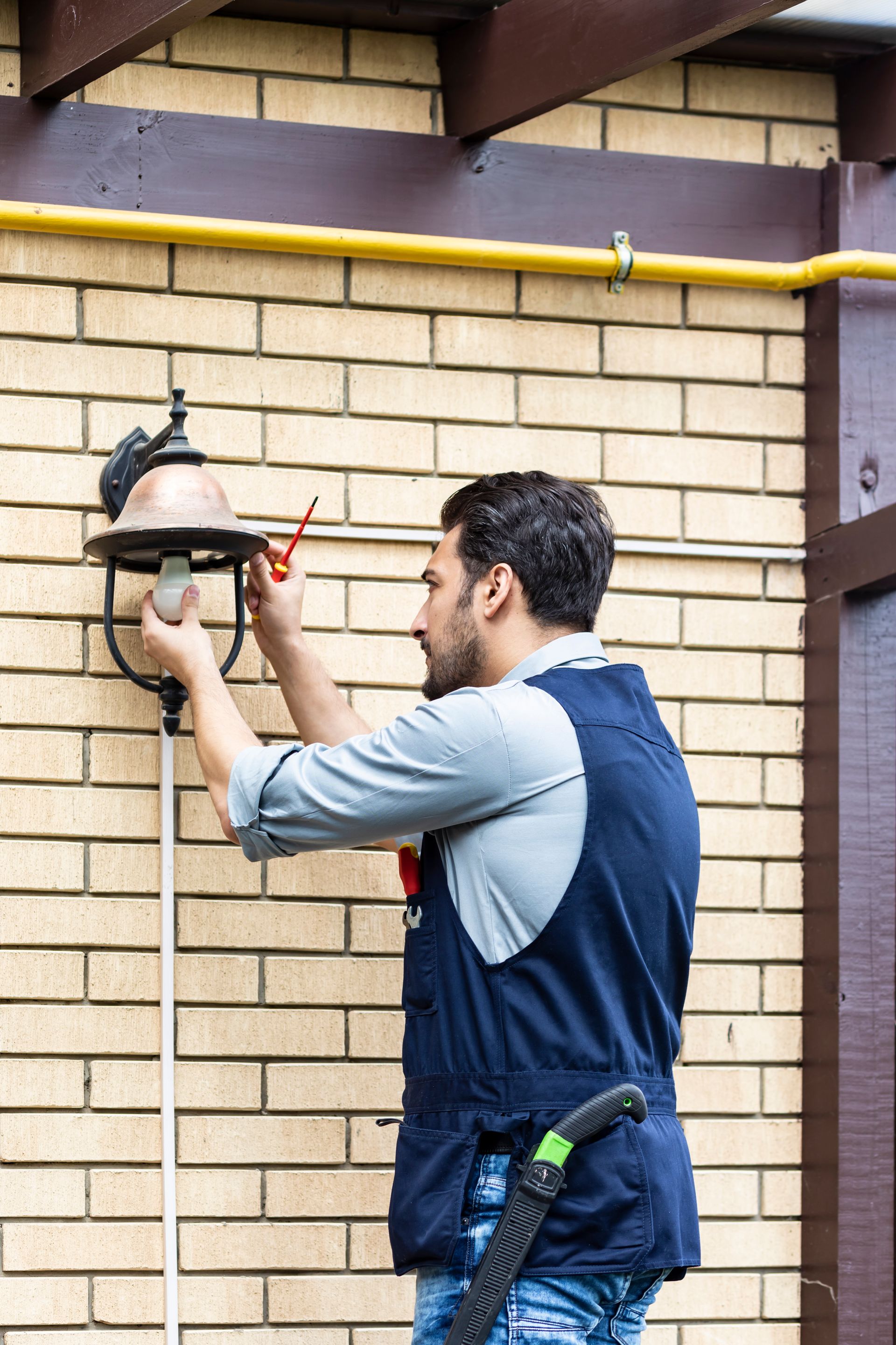 A man is fixing a lamp on a brick wall.