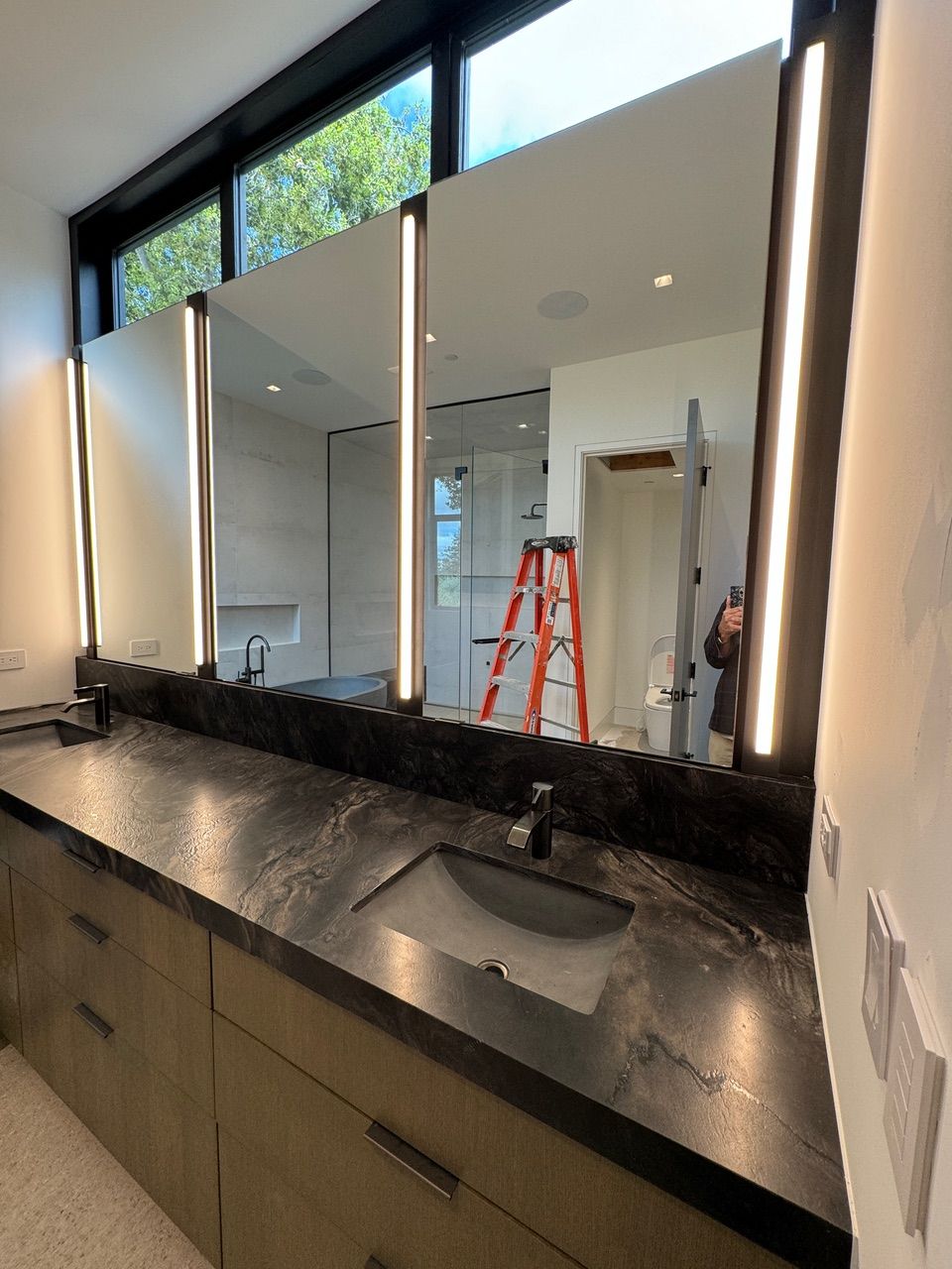 A bathroom with a sink , mirrors and a ladder.