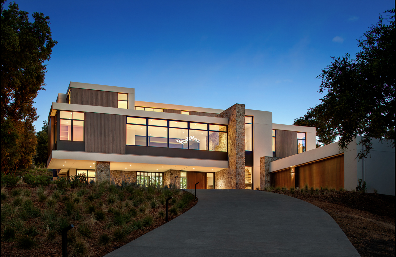 A large modern house with a lot of windows is lit up at night