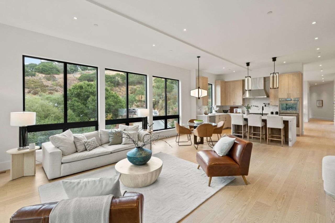 A living room with a couch , chairs , a table and a lot of windows.