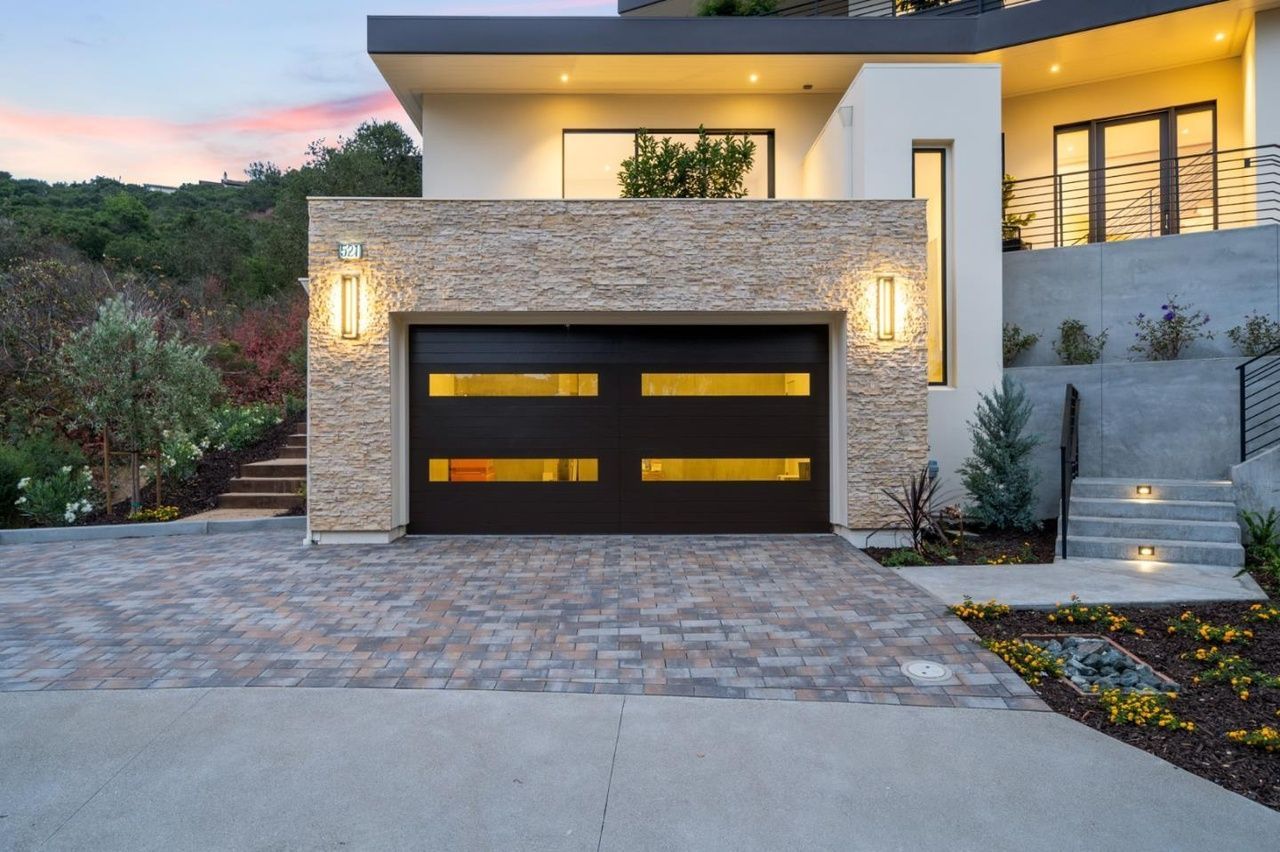 A modern house with a black garage door and a brick driveway.