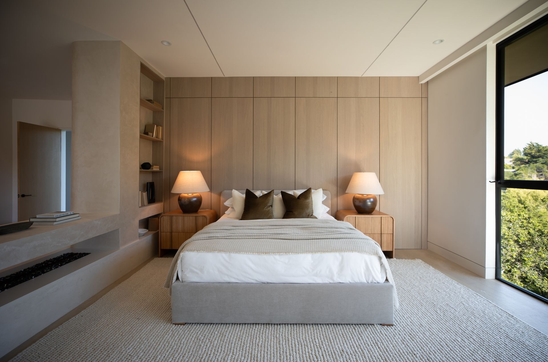 A bedroom with a large bed , two lamps , and a large window.