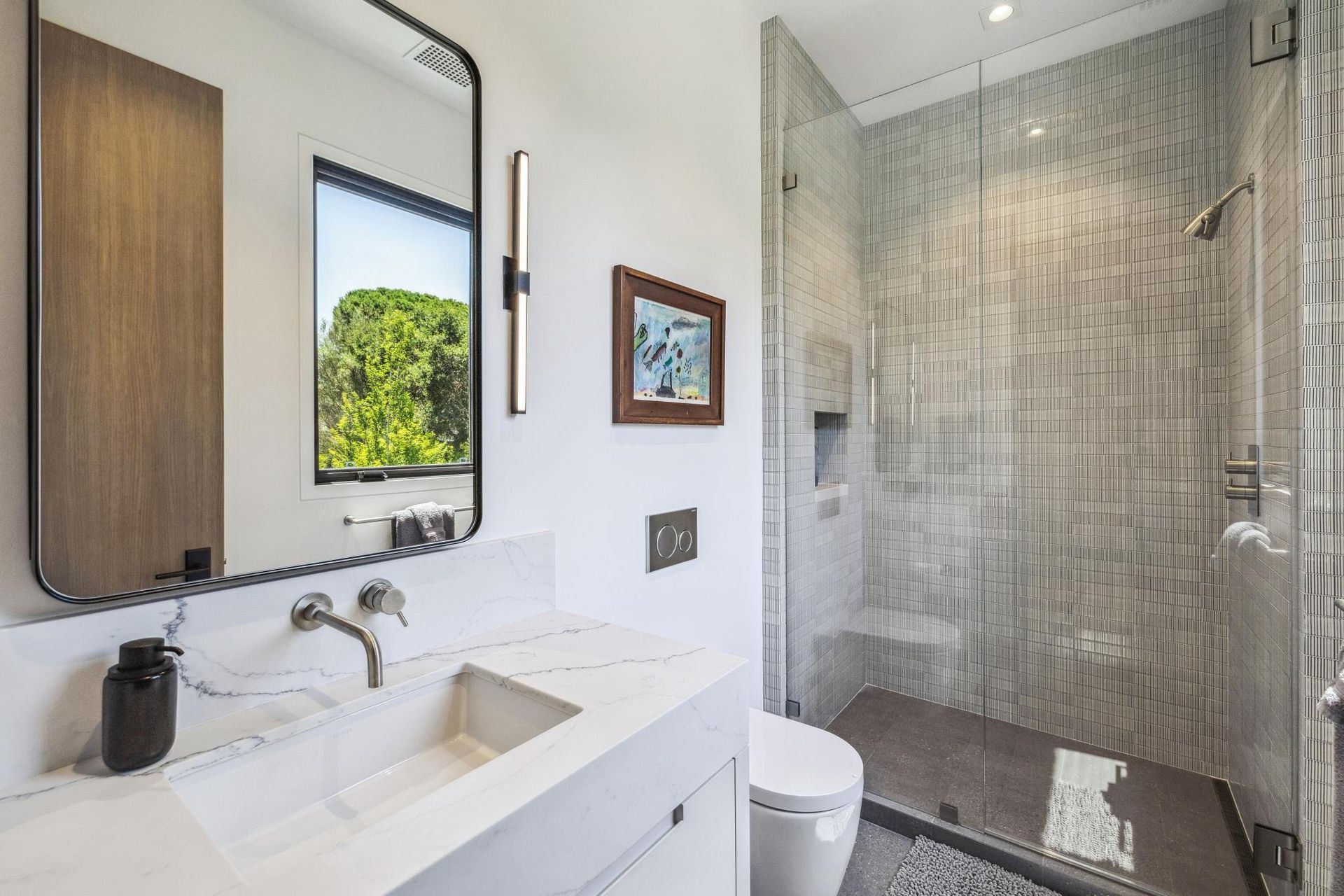 A bathroom with a toilet , sink , mirror and walk in shower.