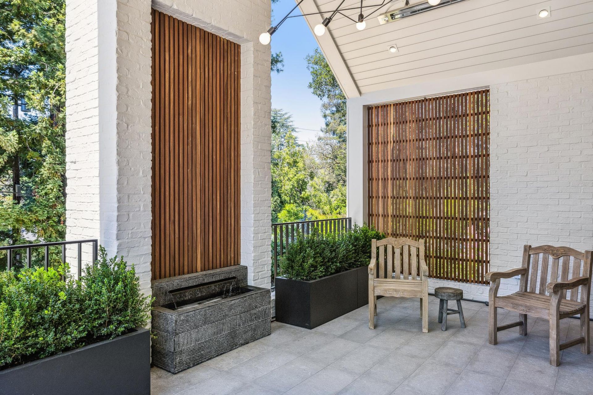 A porch with a wooden wall , chairs , planters and a fountain.