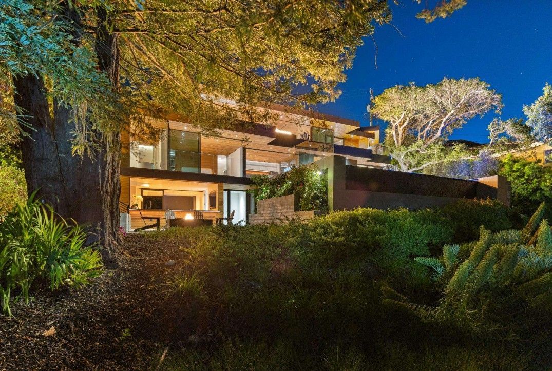 A large house is surrounded by trees and bushes at night.