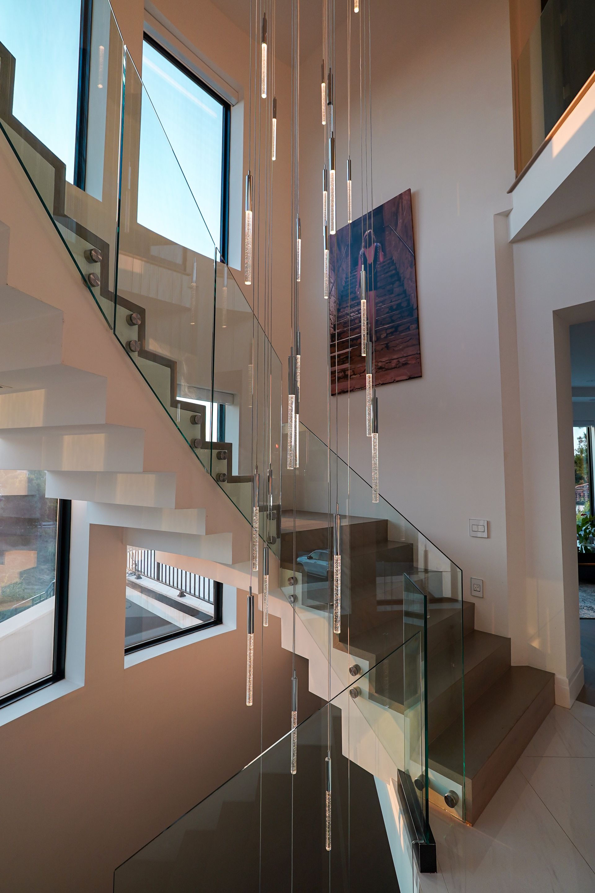 A staircase with a glass railing and a painting on the wall.