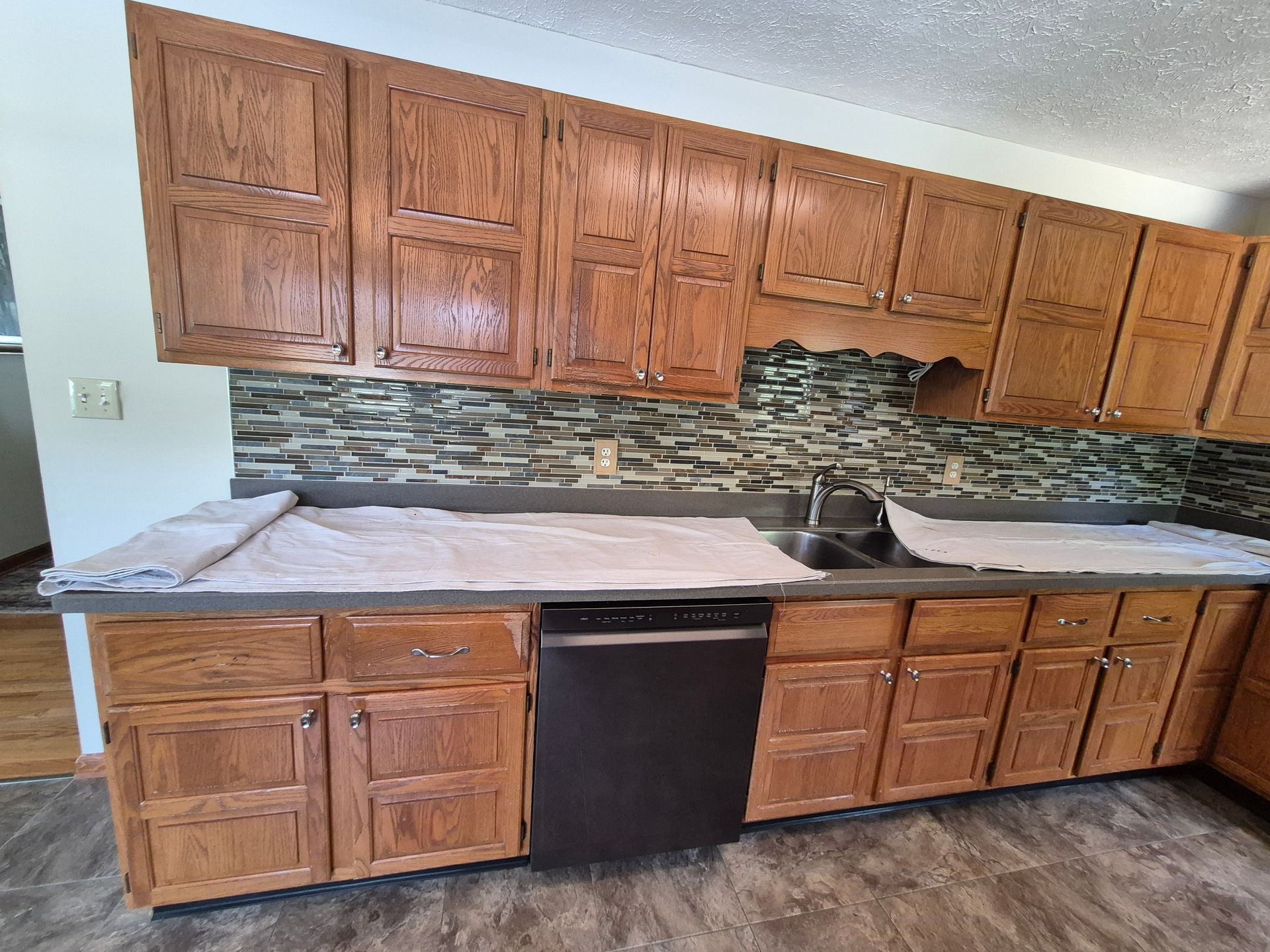 Kitchen with oak cabinets, gray countertops, black appliances, and a decorative tile backsplash.