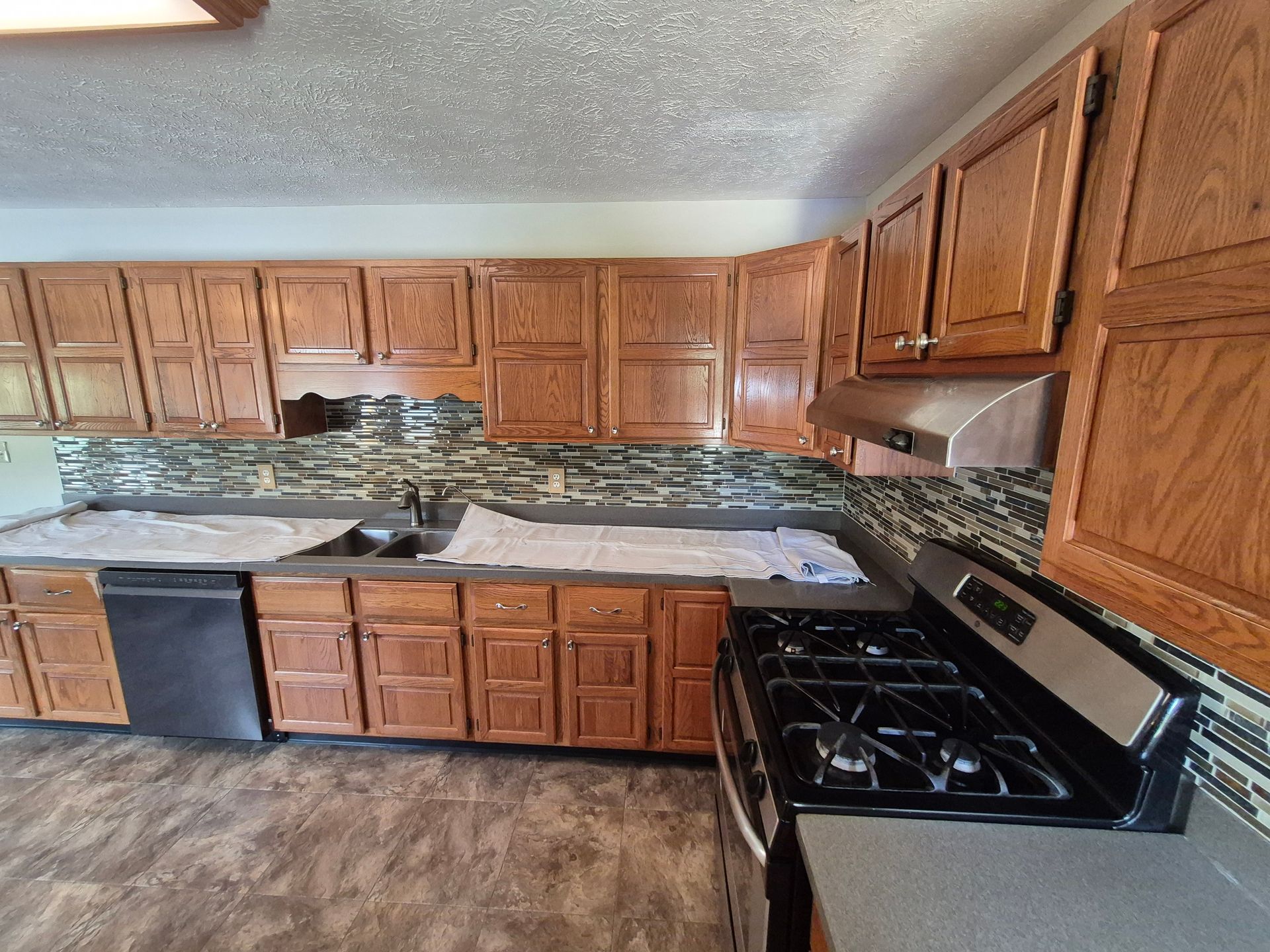 Kitchen with wooden cabinets, dark counters, backsplash, and a stove.