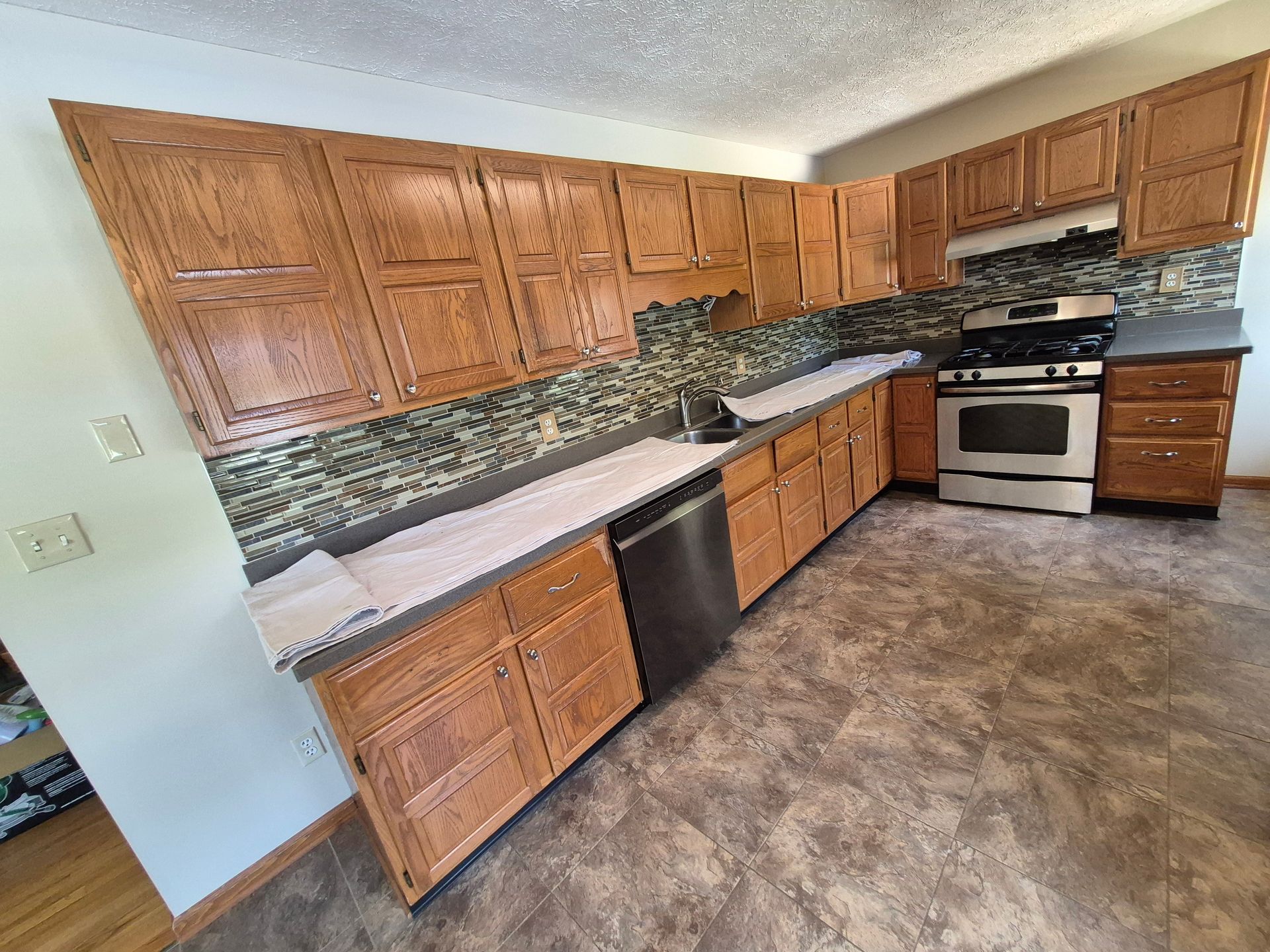 A kitchen with light brown cabinets, a stainless steel range, and mosaic backsplash.
