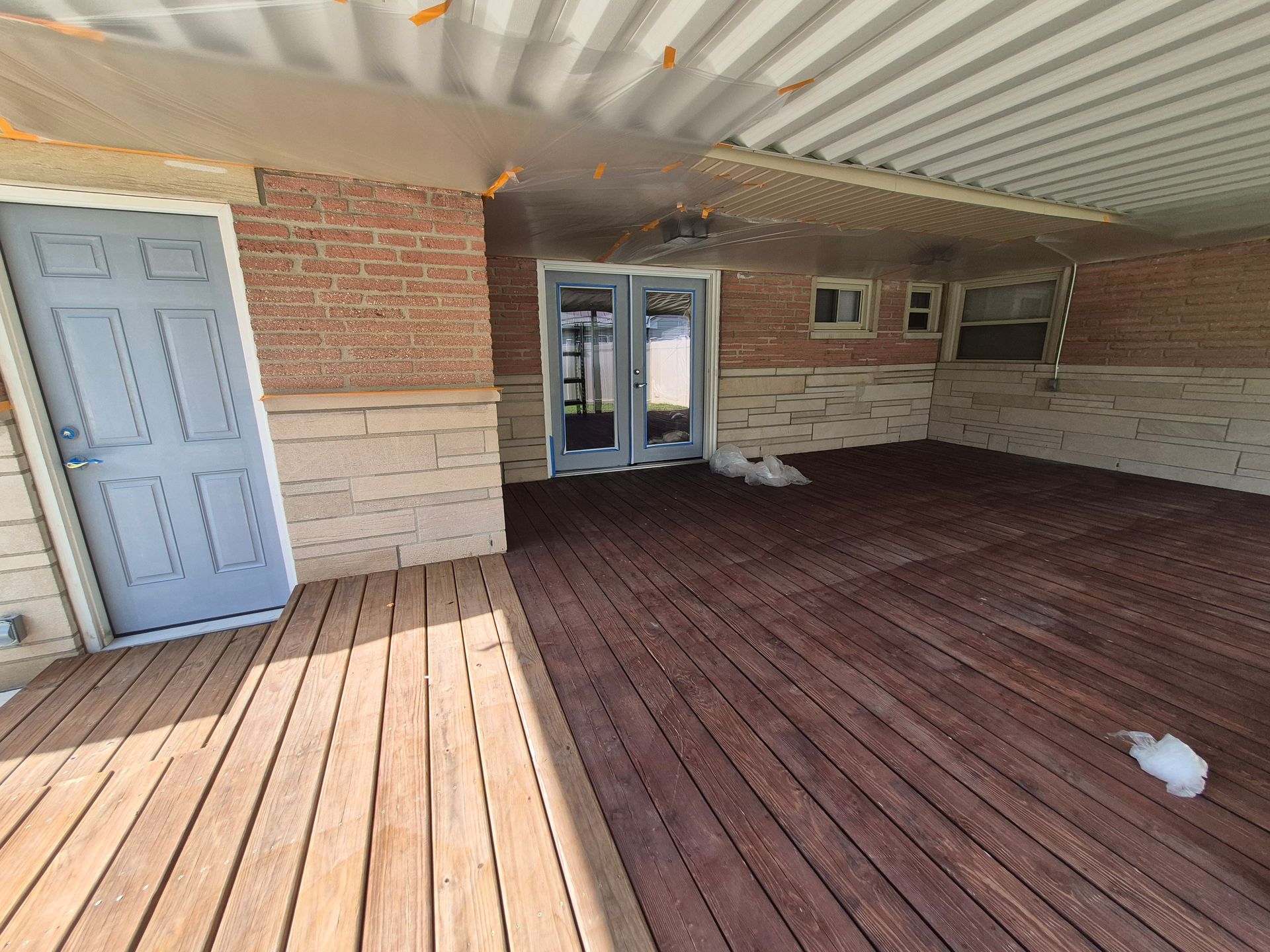 Wooden deck with a blue door, red brick wall, and glass doors.
