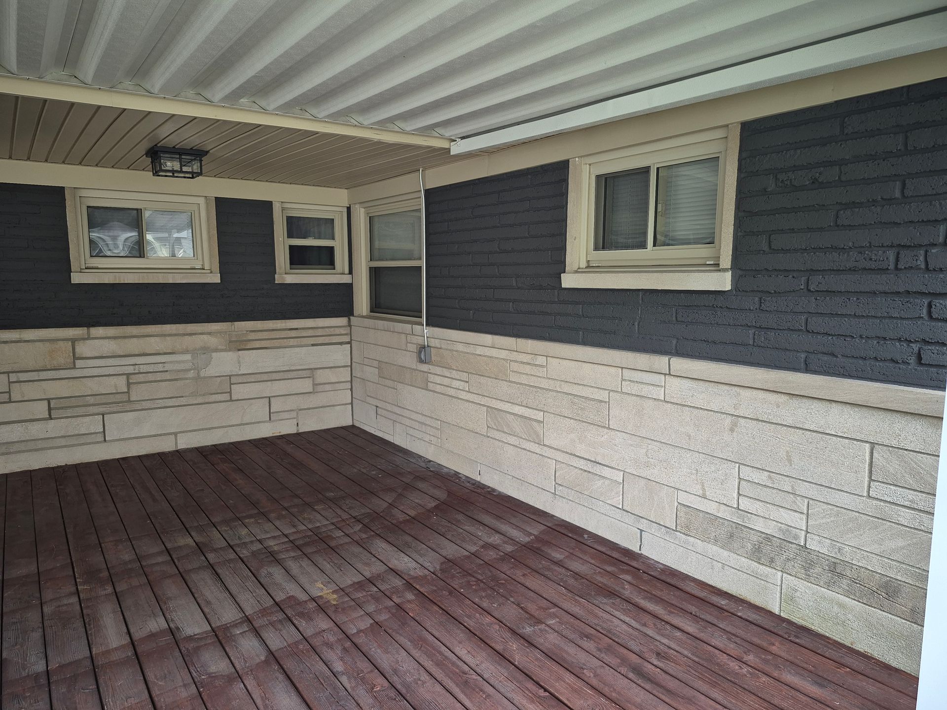 Covered porch with dark wooden floor, light stone accent wall, and dark gray siding.