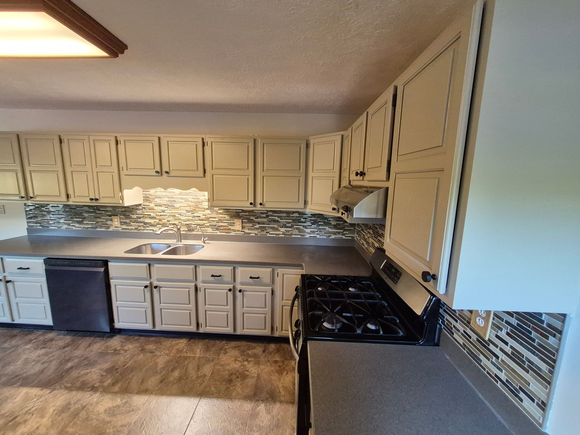 Kitchen with cream cabinets, black appliances, gray counters, and a mirrored backsplash.