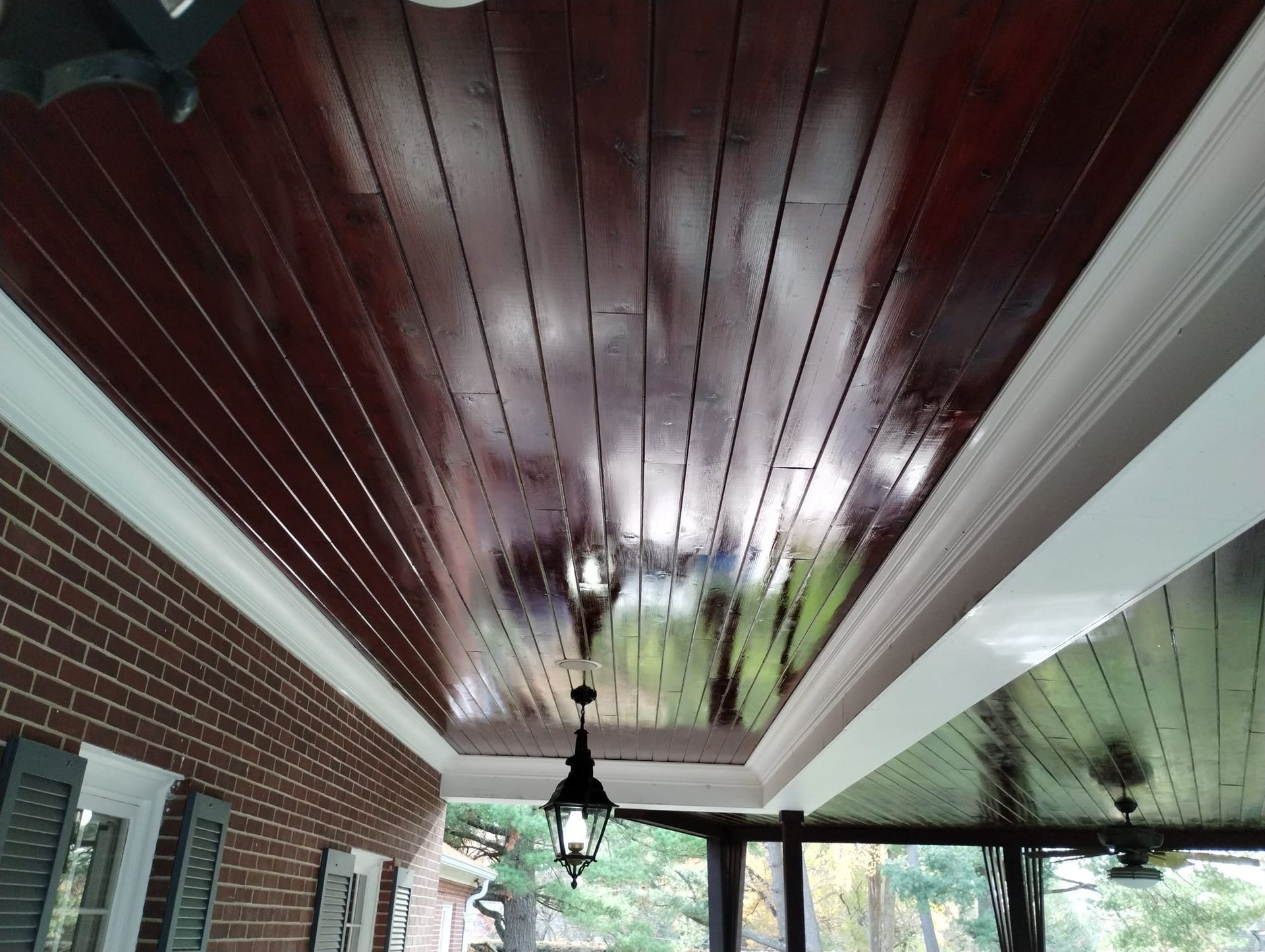 Red-stained wood porch ceiling with white trim, a black lantern, and a brick wall.