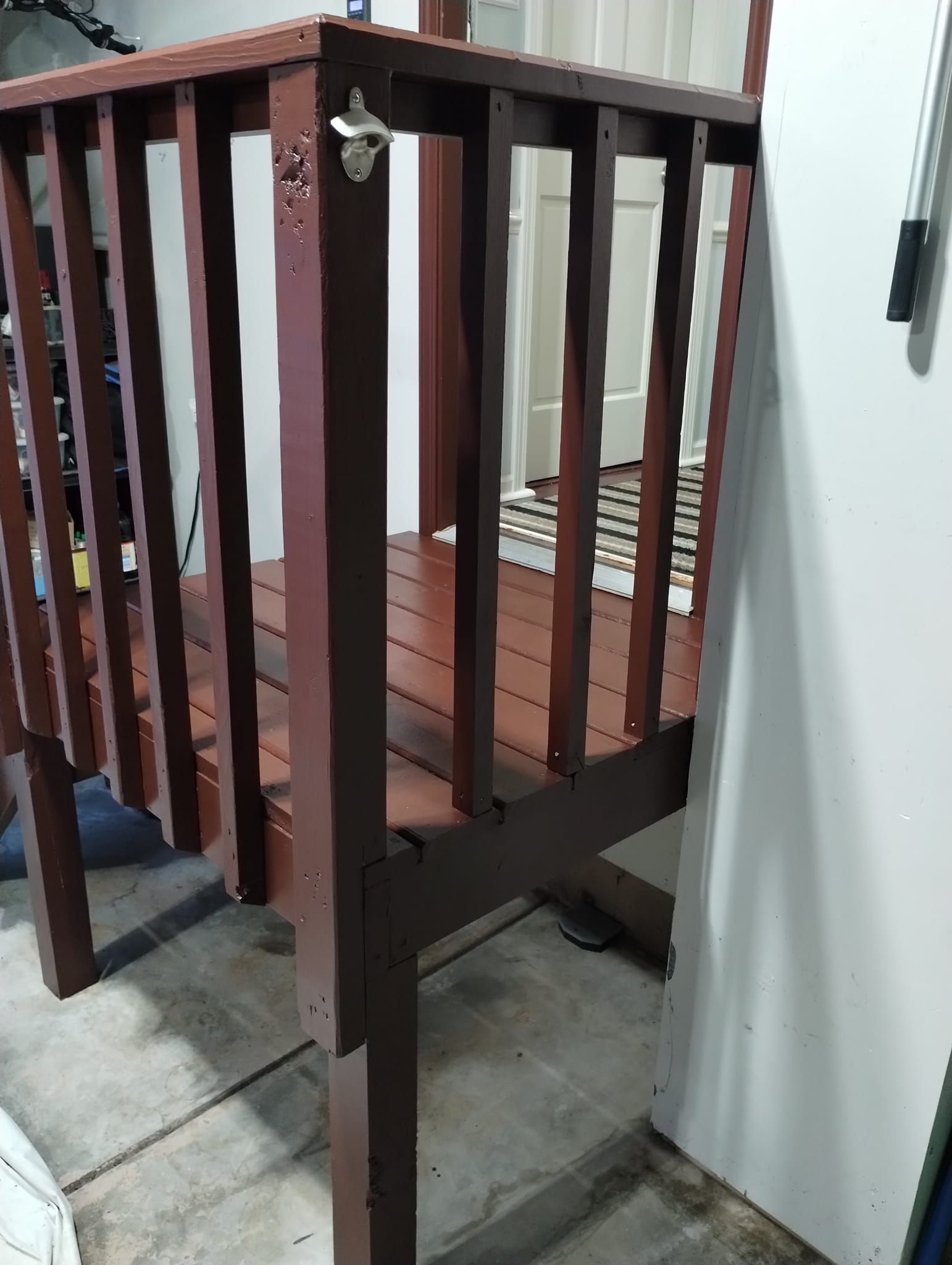 Wooden deck with bottle opener attached. Brown stain. Garage setting.